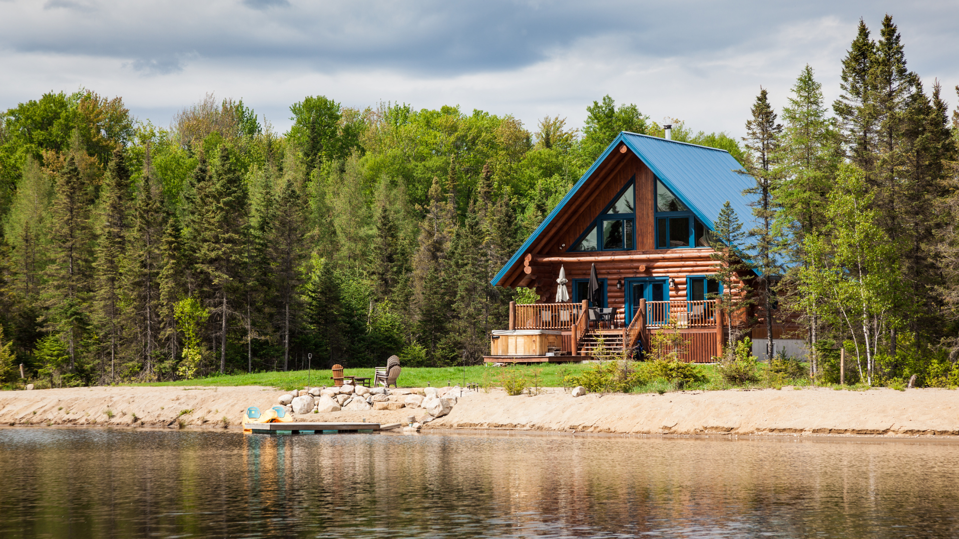 A log cabin with a balcony and a carport in the woods.