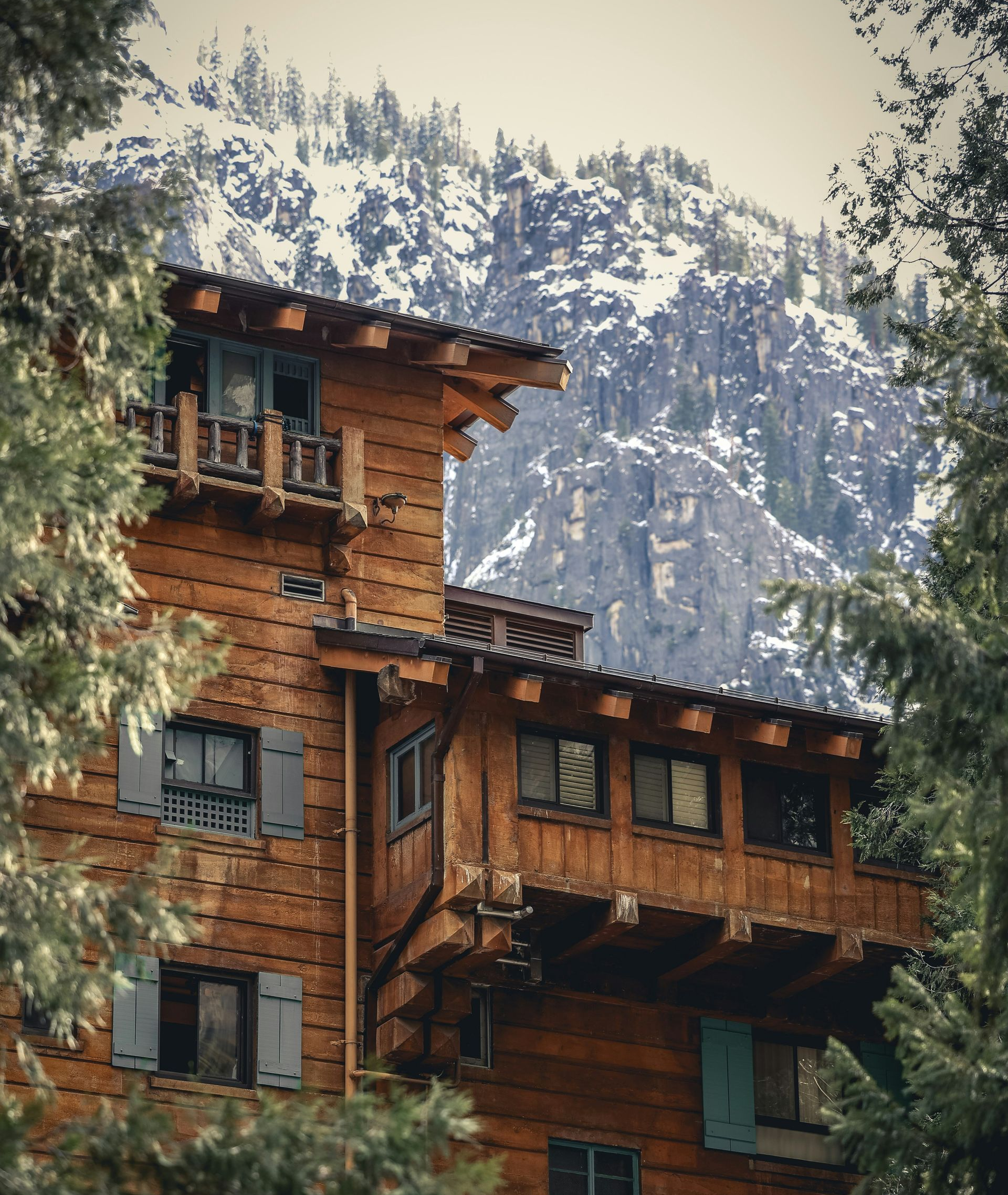 Rustic wooden mountain lodge with balconies amid pine trees and snowy peaks