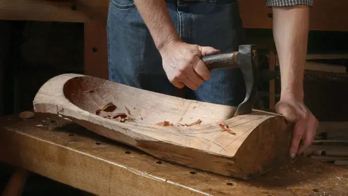 Person carving a wooden bowl with a hammer and chisel on a workbench