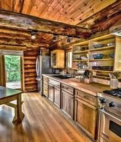 Rustic log cabin kitchen with wooden cabinets, stainless appliances, and warm wood ceiling