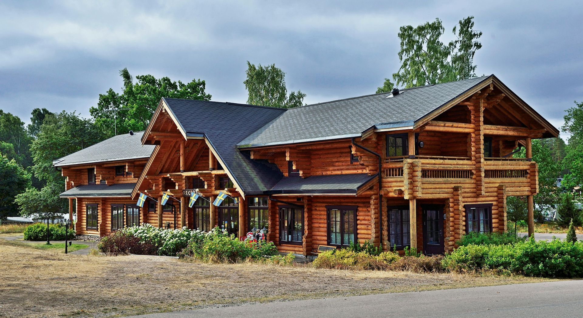 Log cabin lodge with large wooden porches, dark roof, and landscaped grounds under a cloudy sky