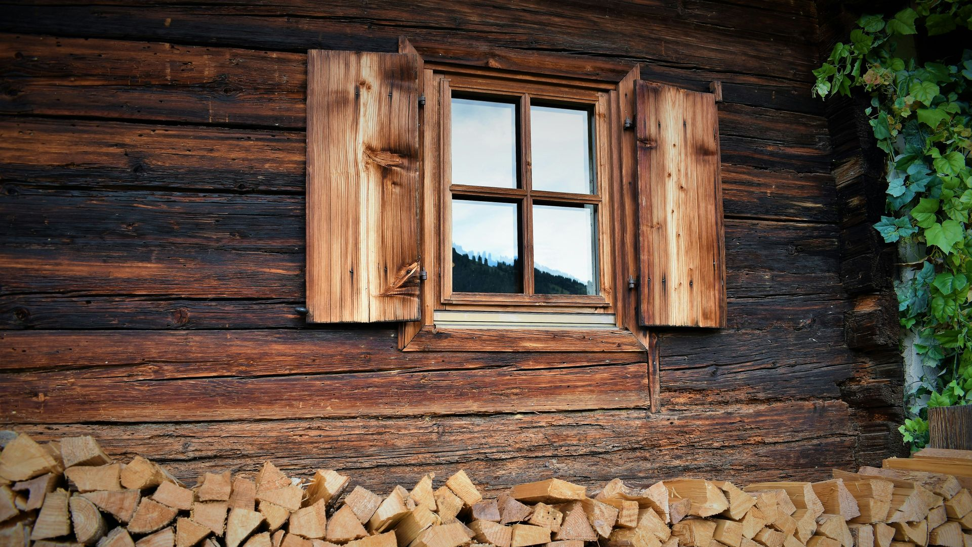 Rustic wooden cabin wall with a window and stacked firewood underneath