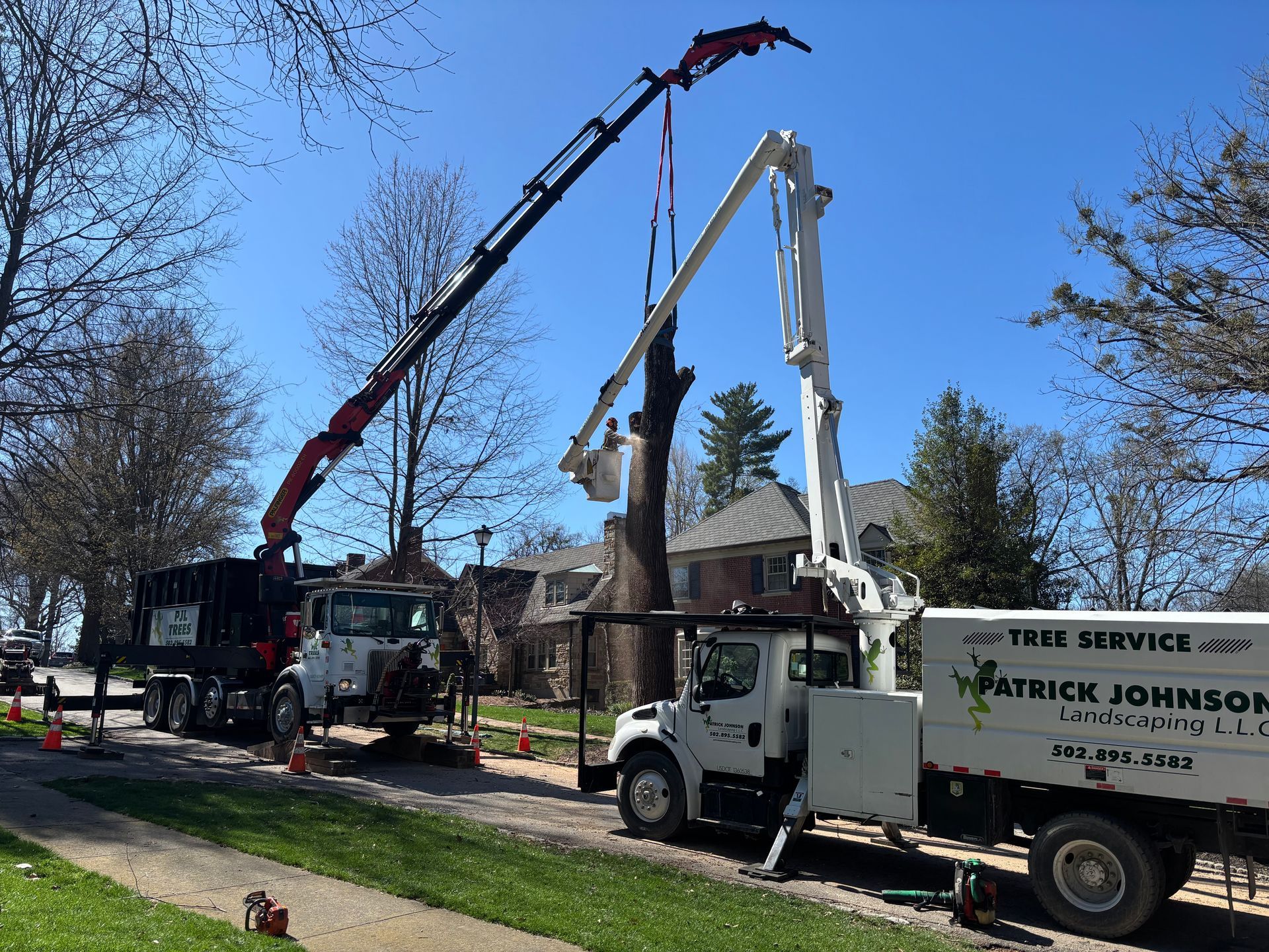Two utility trucks lift a long yellow beam over a residential street.