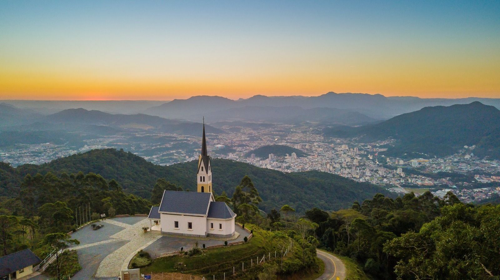Igreja no alto de uma colina com vista para a cidade ao pôr do sol; céu azul e amarelo.