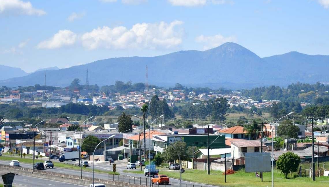 Paisagem urbana com montanhas ao fundo, sob um céu azul com nuvens dispersas.