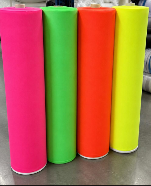 Cuatro alfombras enrolladas altas de color rosa, verde, naranja y amarillo, colocadas sobre un piso.