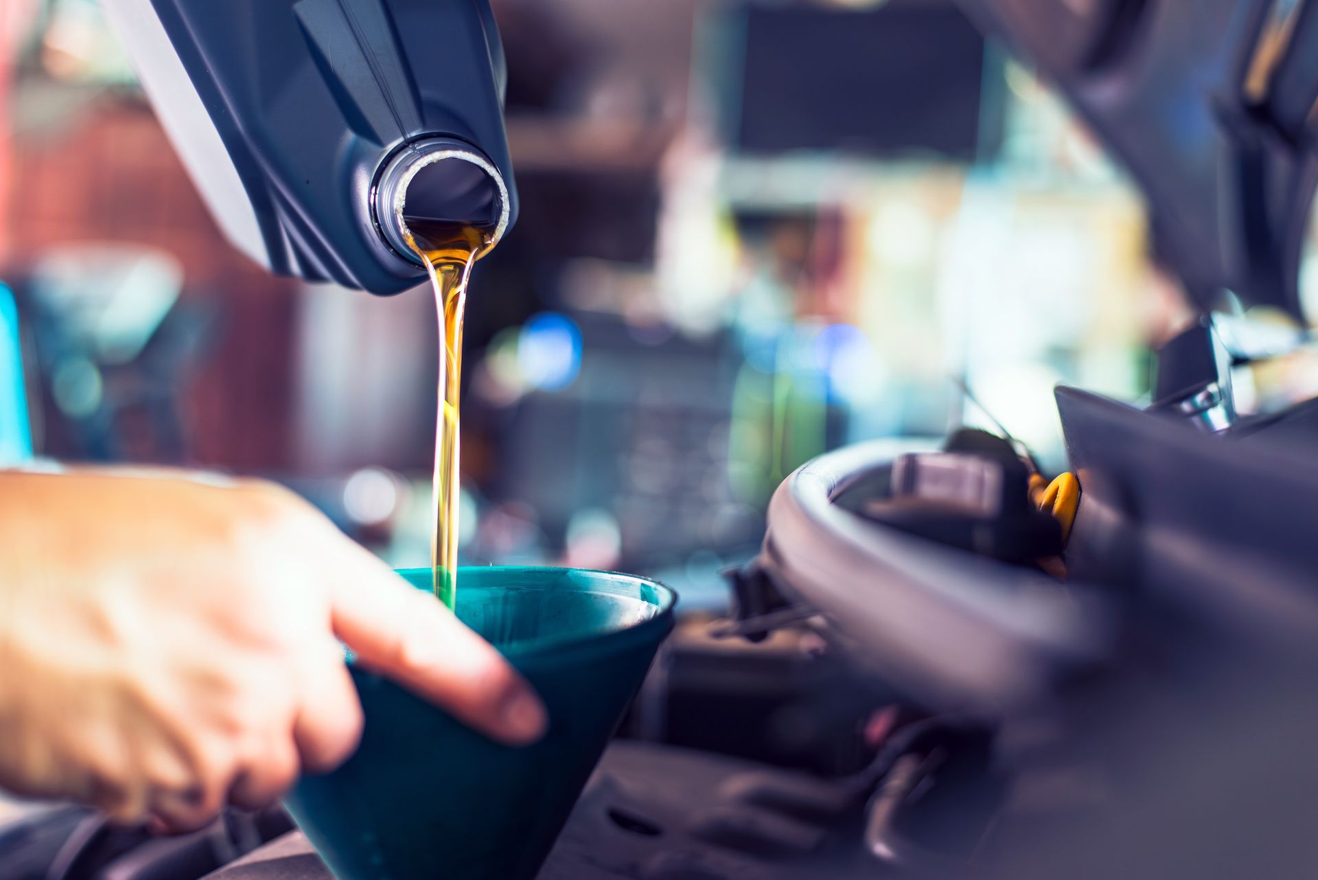 Fuel pouring into a car at a gas station, with a hand holding the nozzle over a green funnel.