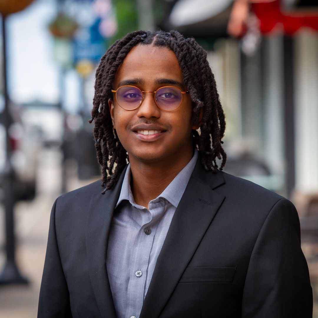 A man with dreadlocks is wearing a suit and tie and smiling.