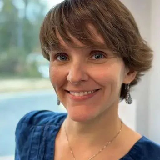 A woman wearing a blue shirt and a necklace is smiling for the camera.