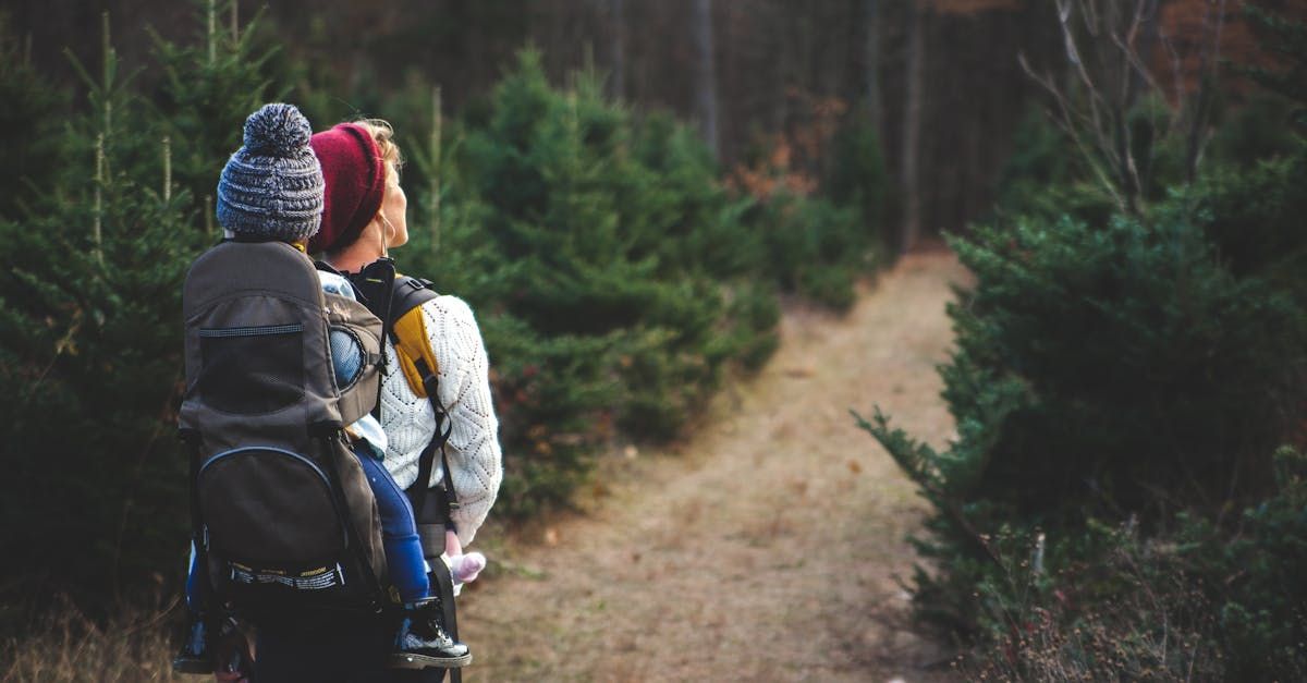 A woman is carrying a baby in a backpack on a path in the woods.