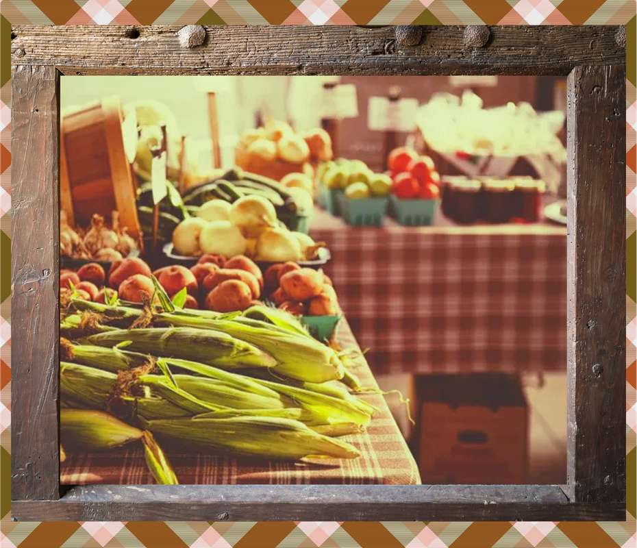 Farmers market stall with fresh corn, tomatoes, and other produce on checkered tablecloths.
