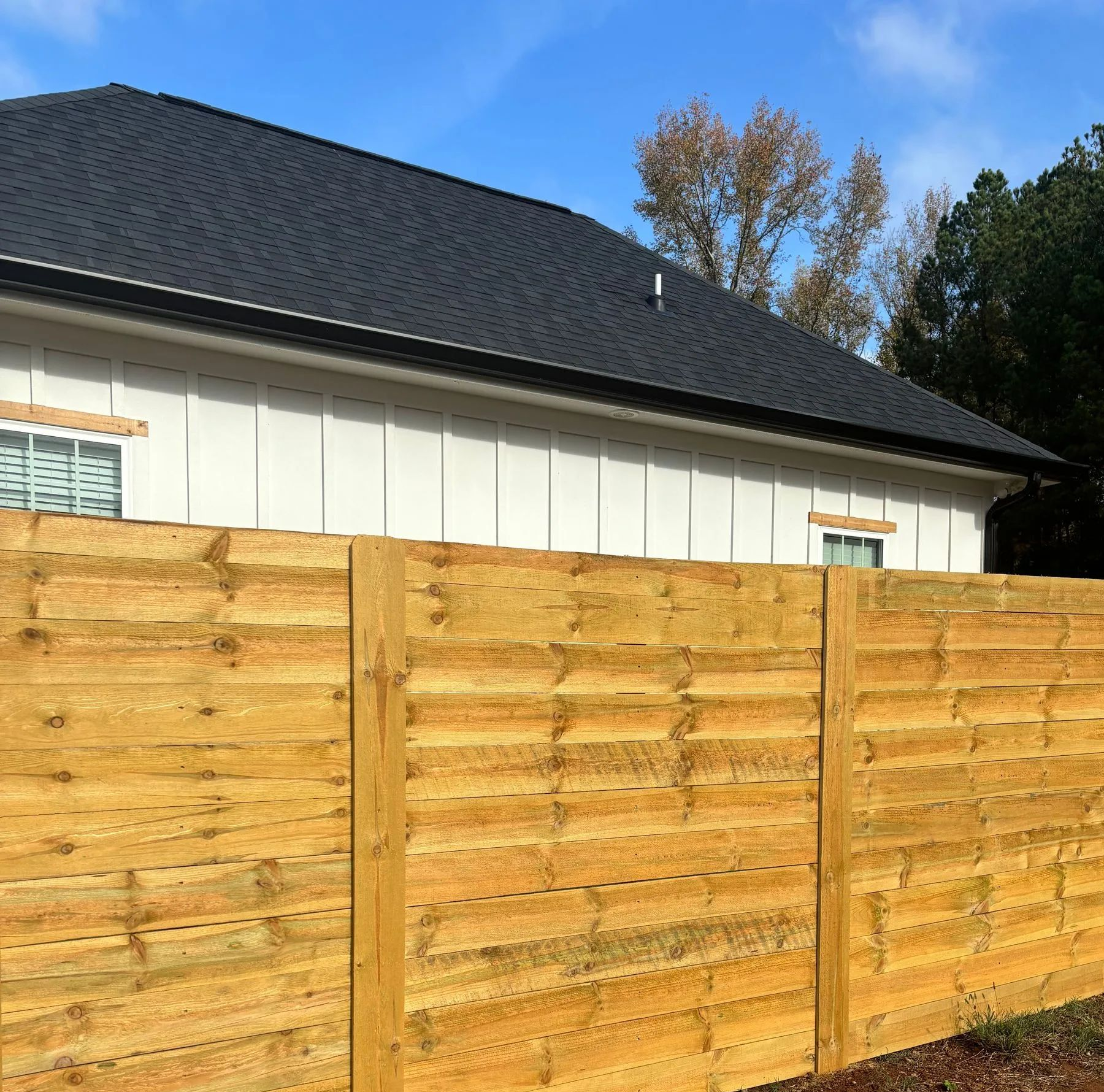 Wooden fence in front of a white house with a dark roof under a blue sky