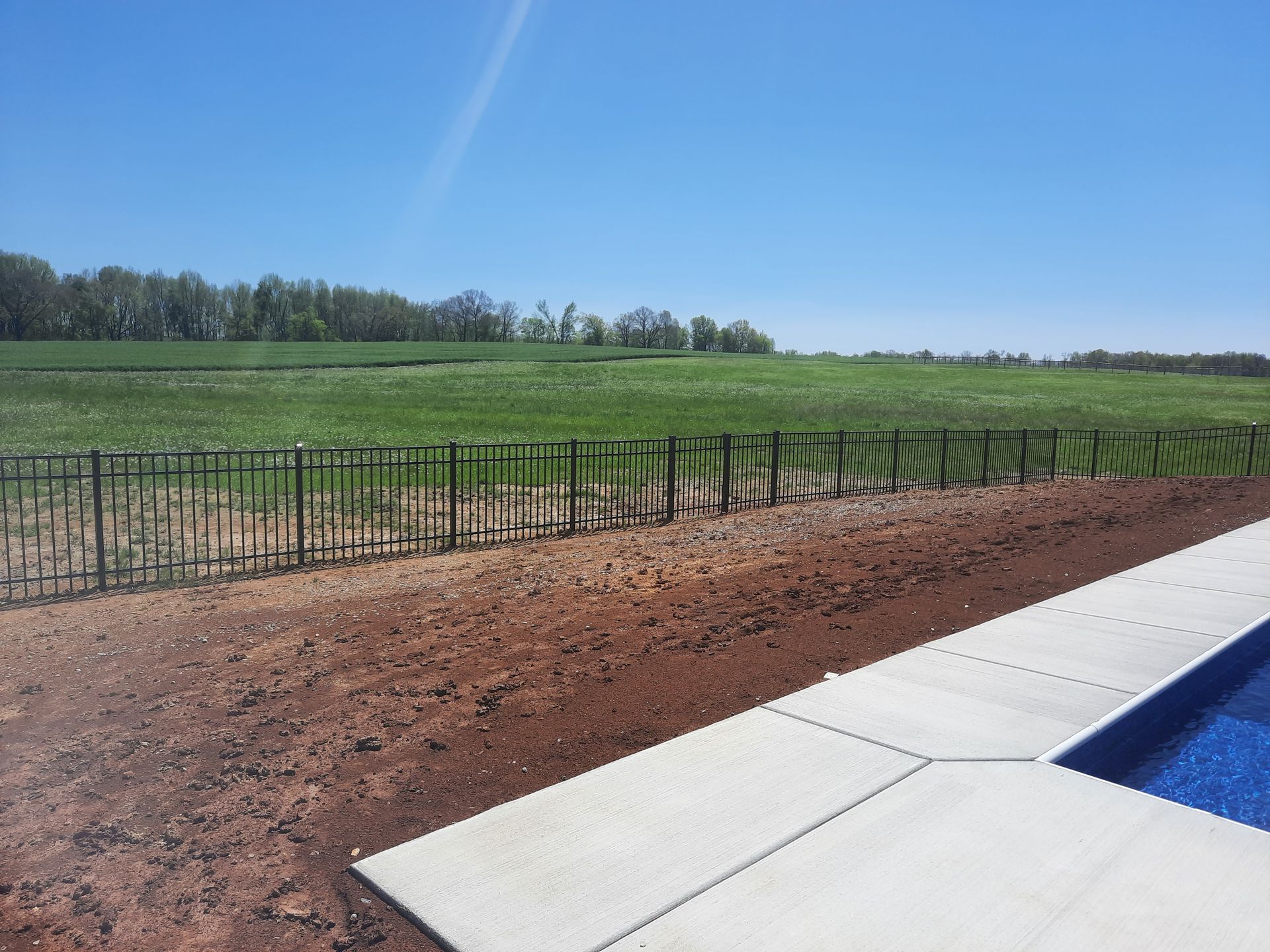 A fence surrounds a swimming pool with a field in the background