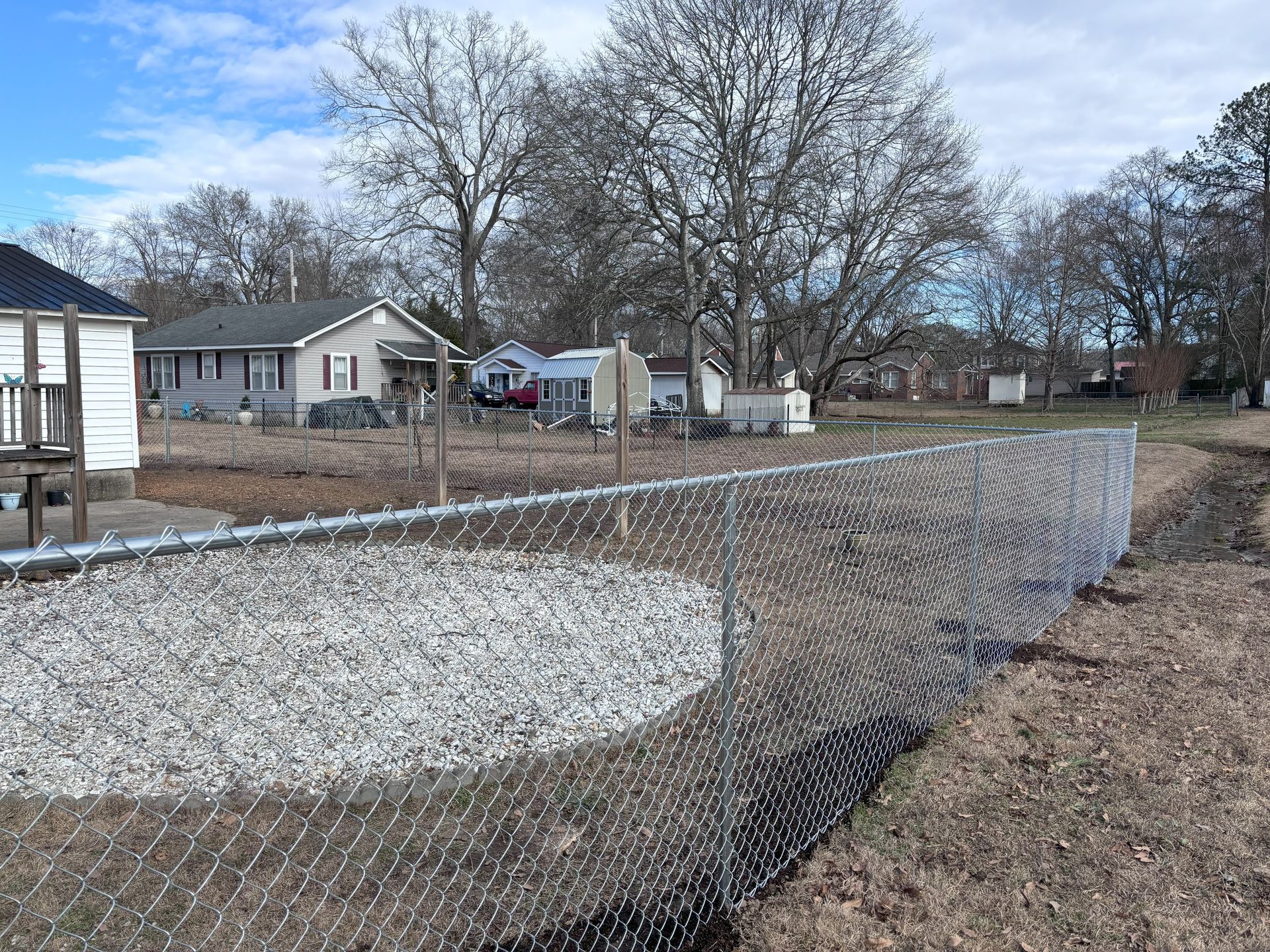 A chain link fence surrounds a yard with a house in the background.