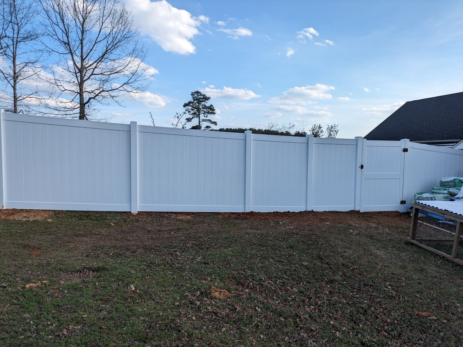 A white fence with a gate in the backyard of a house.