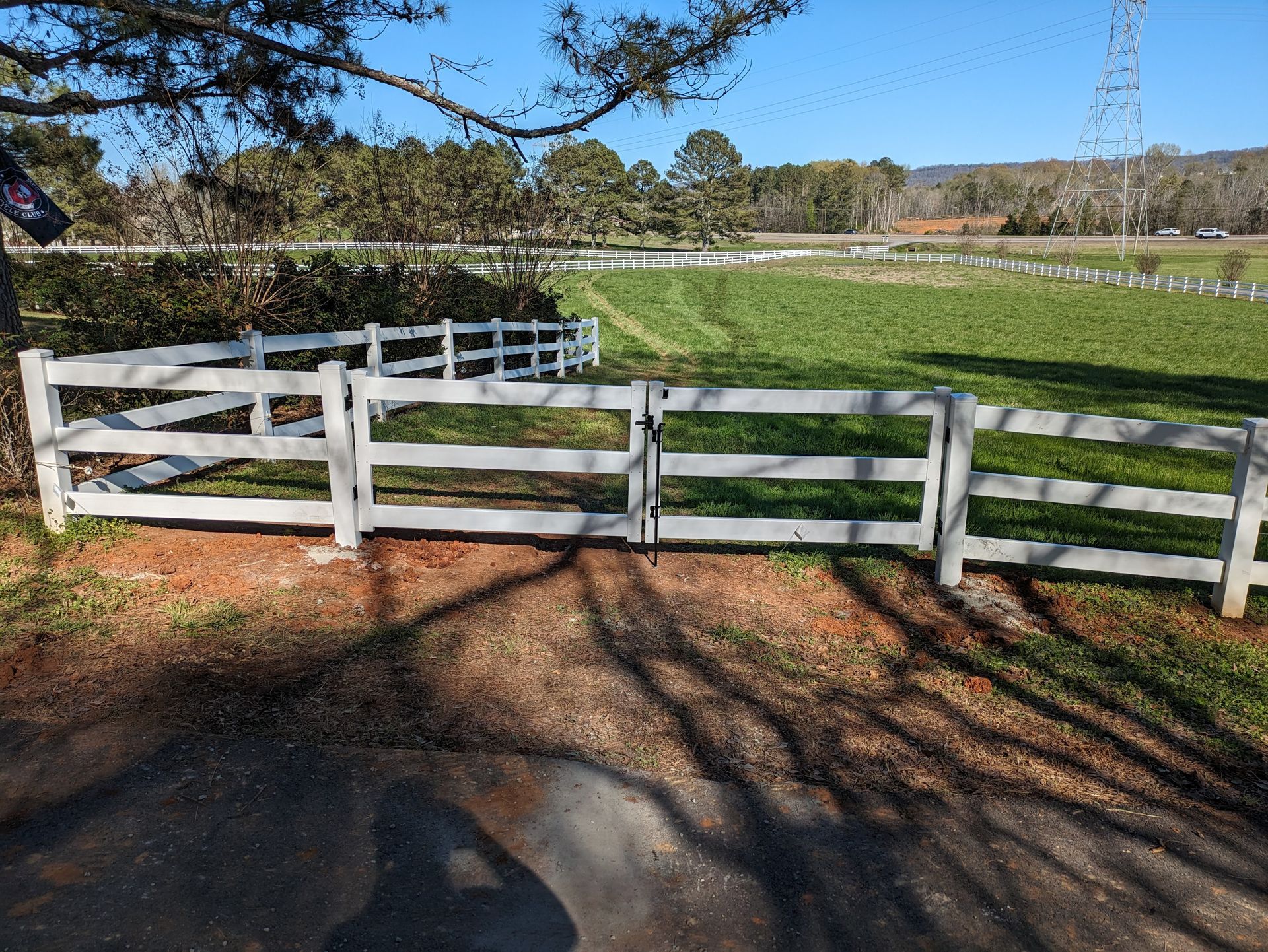 A white fence surrounds a grassy field on a sunny day.