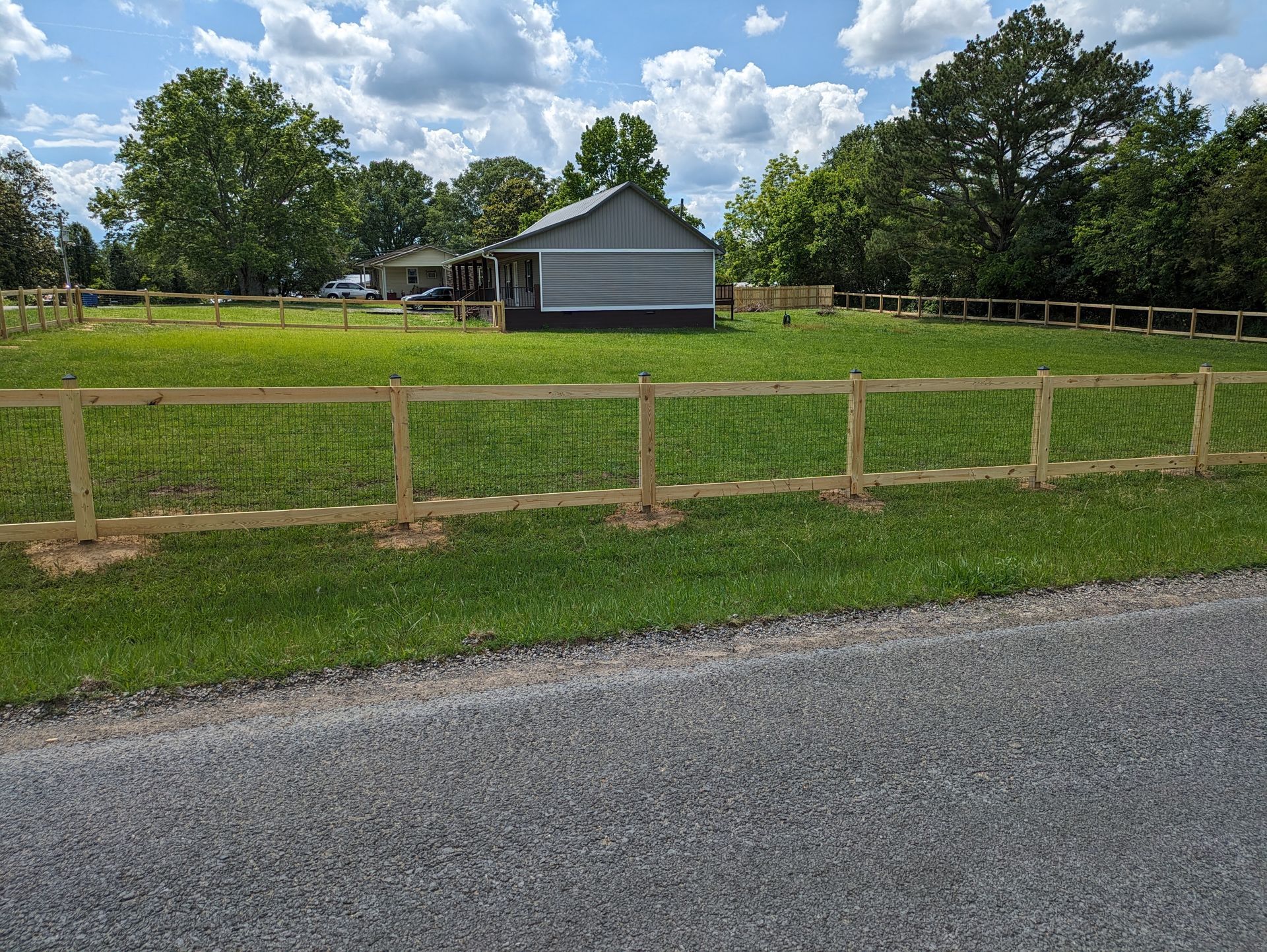 A wooden fence surrounds a grassy field with a house in the background.