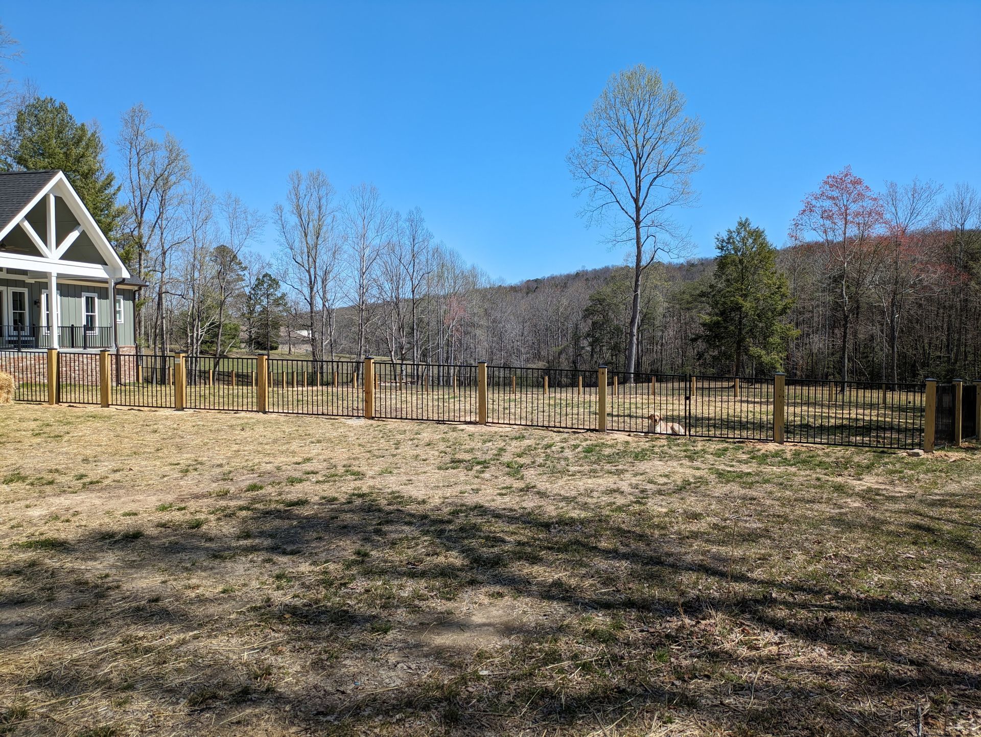 A wooden fence surrounds a grassy field in front of a house.