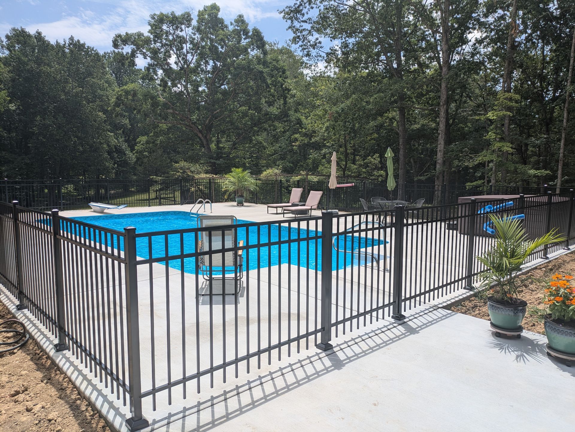 A fence surrounds a large swimming pool in a backyard.