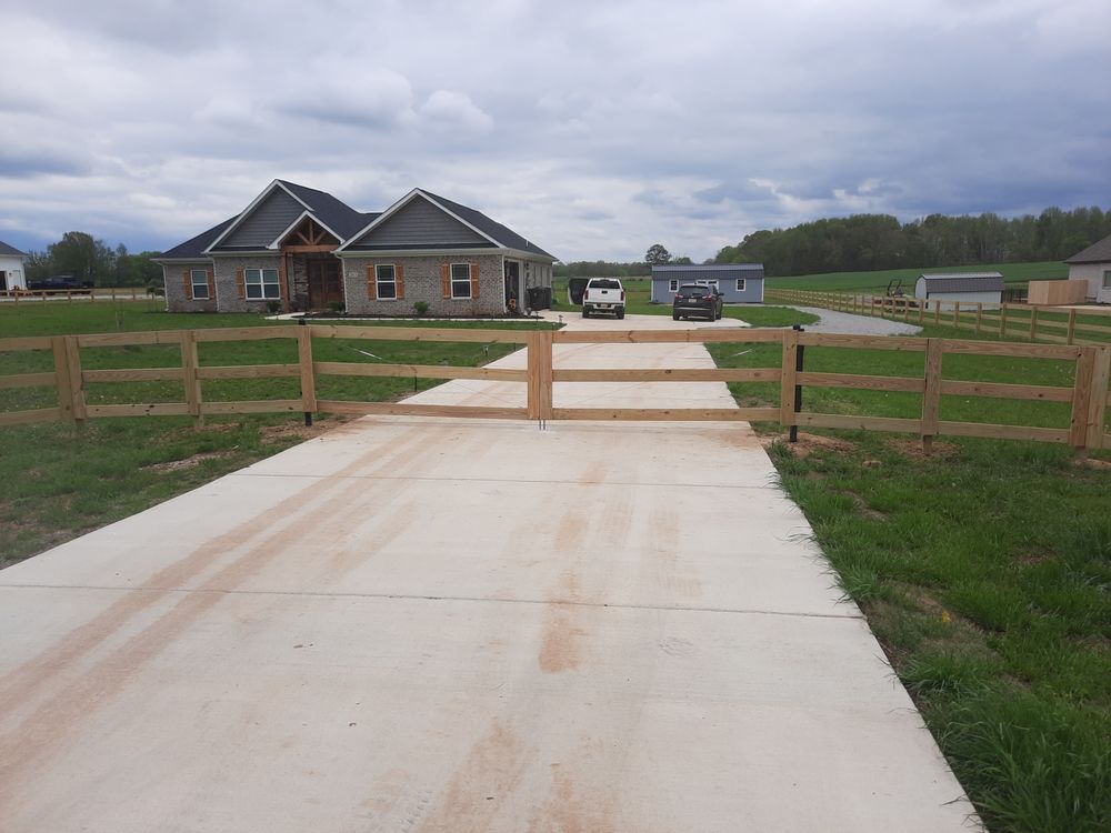 A wooden fence surrounds a driveway leading to a house.