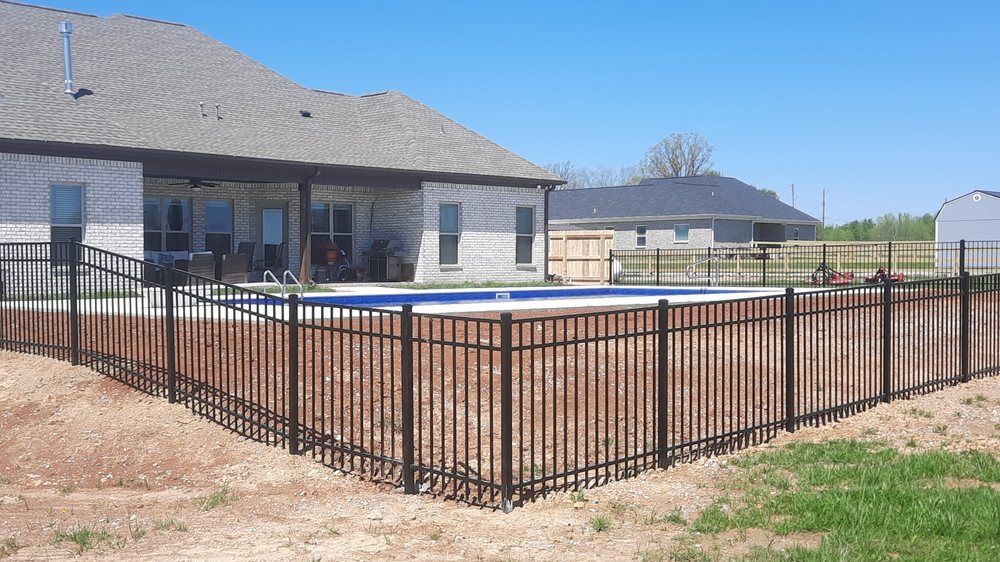 A metal fence surrounds a swimming pool in front of a house.