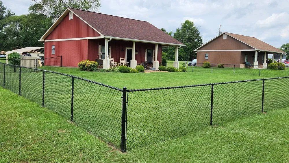 Red house and tan house behind a black chain-link fence on a grassy lawn.