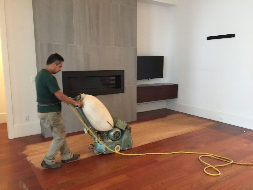 Technician sanding hardwood in a modern living room of a Virginia Beach home
