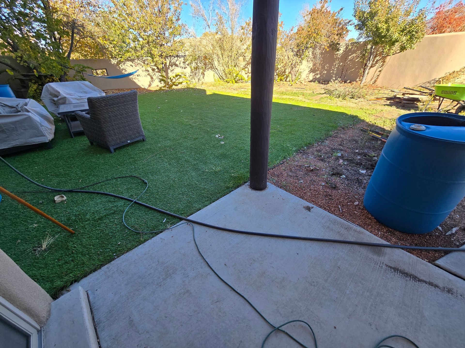 A blue barrel is sitting on the ground in a backyard.