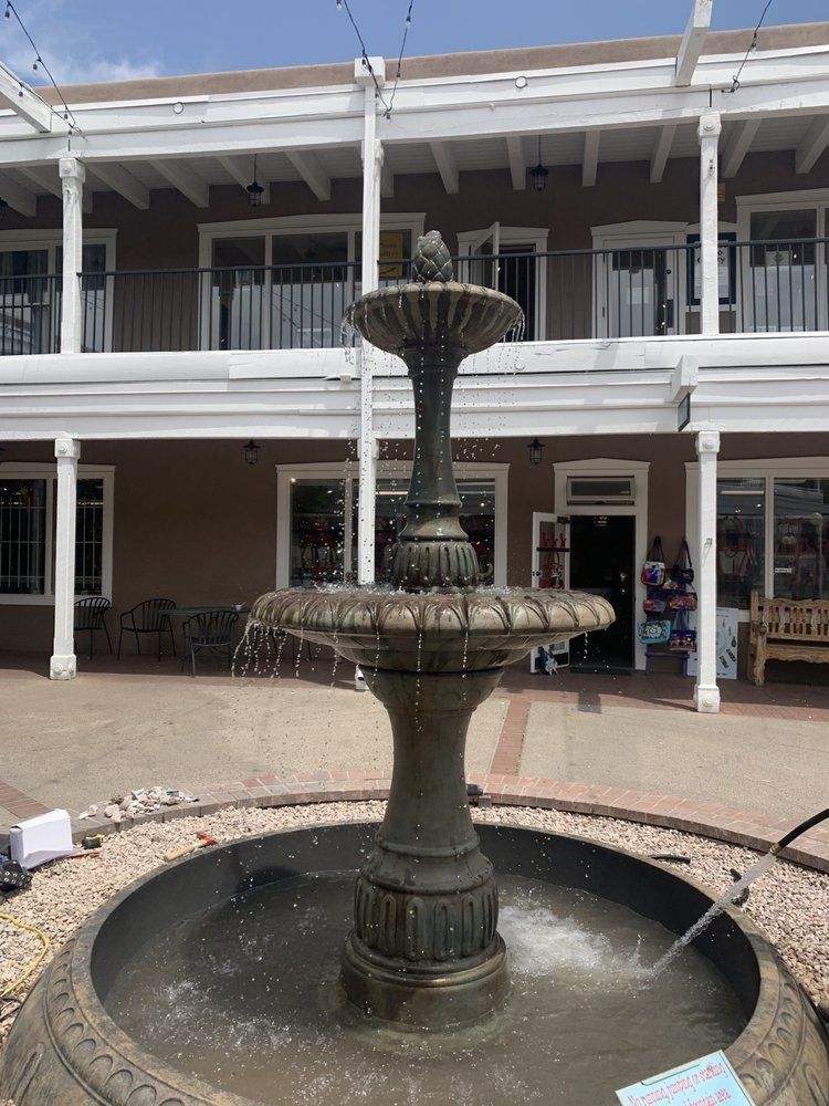 A fountain is in the middle of a courtyard in front of a building.