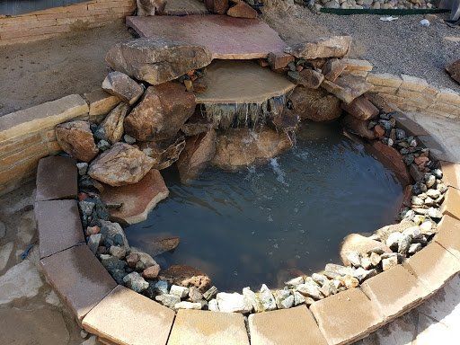 A small pond surrounded by rocks and bricks with a waterfall in the middle.