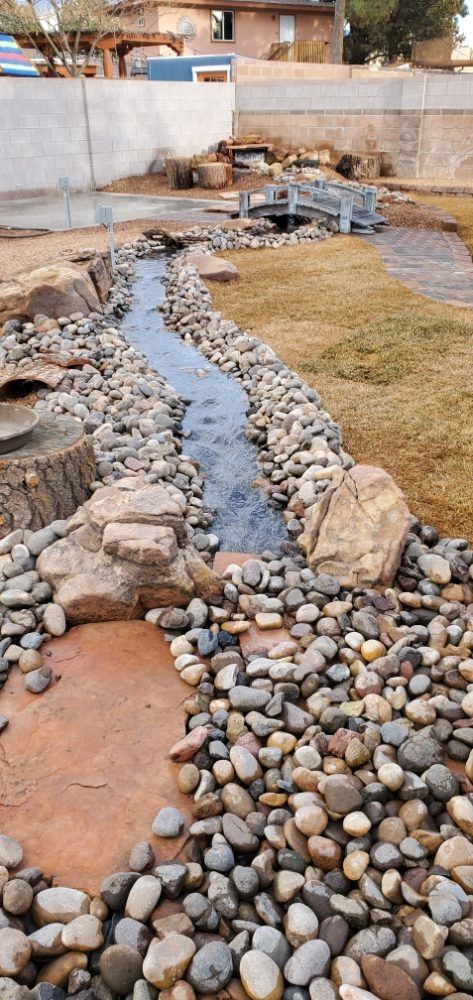 A stream is surrounded by rocks and grass in a backyard.