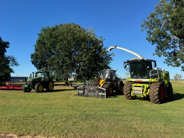Two people shaking hands in front of a yellow combine harvester in a field.