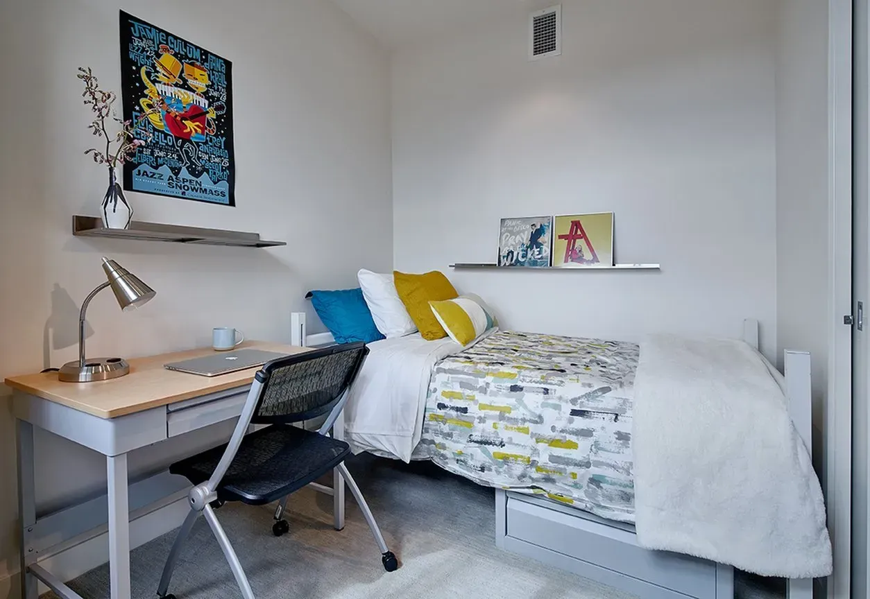 A bedroom with a bed , desk , chair and lamp.