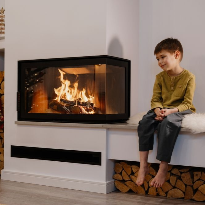 Child sitting beside a modern corner fireplace with burning logs in a living room