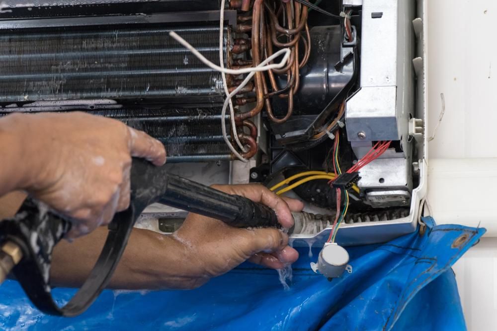 A Person Is Cleaning an Air Conditioner with A Spray Bottle — Northernair in Mullumbimby, NSW
