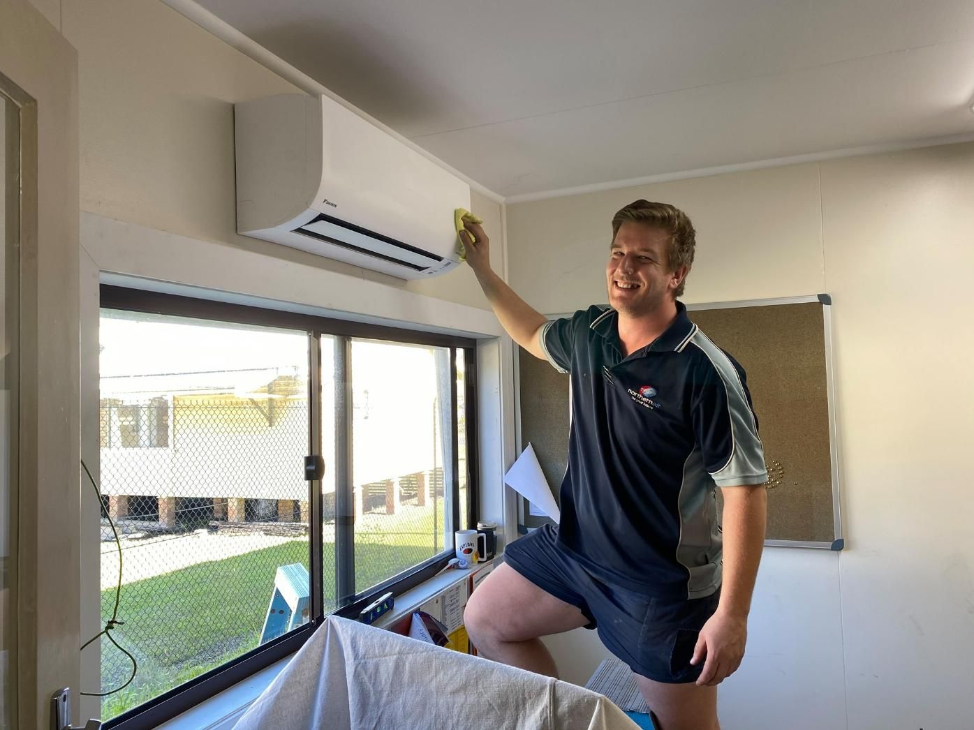 A Man Is Cleaning an Air Conditioner with A Sponge in A Room — Northernair in Lismore, NSW