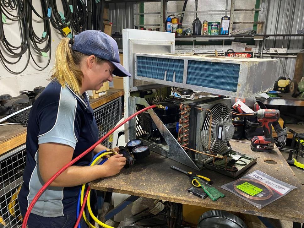 A Woman Is Working on An Air Conditioner in A Garage — Northernair in Ocean Shores, NSW