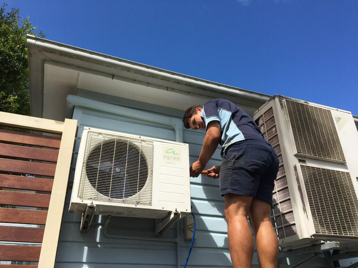 A Man Is Working on An Air Conditioner on The Side of A House — Northernair in Evans Head, NSW