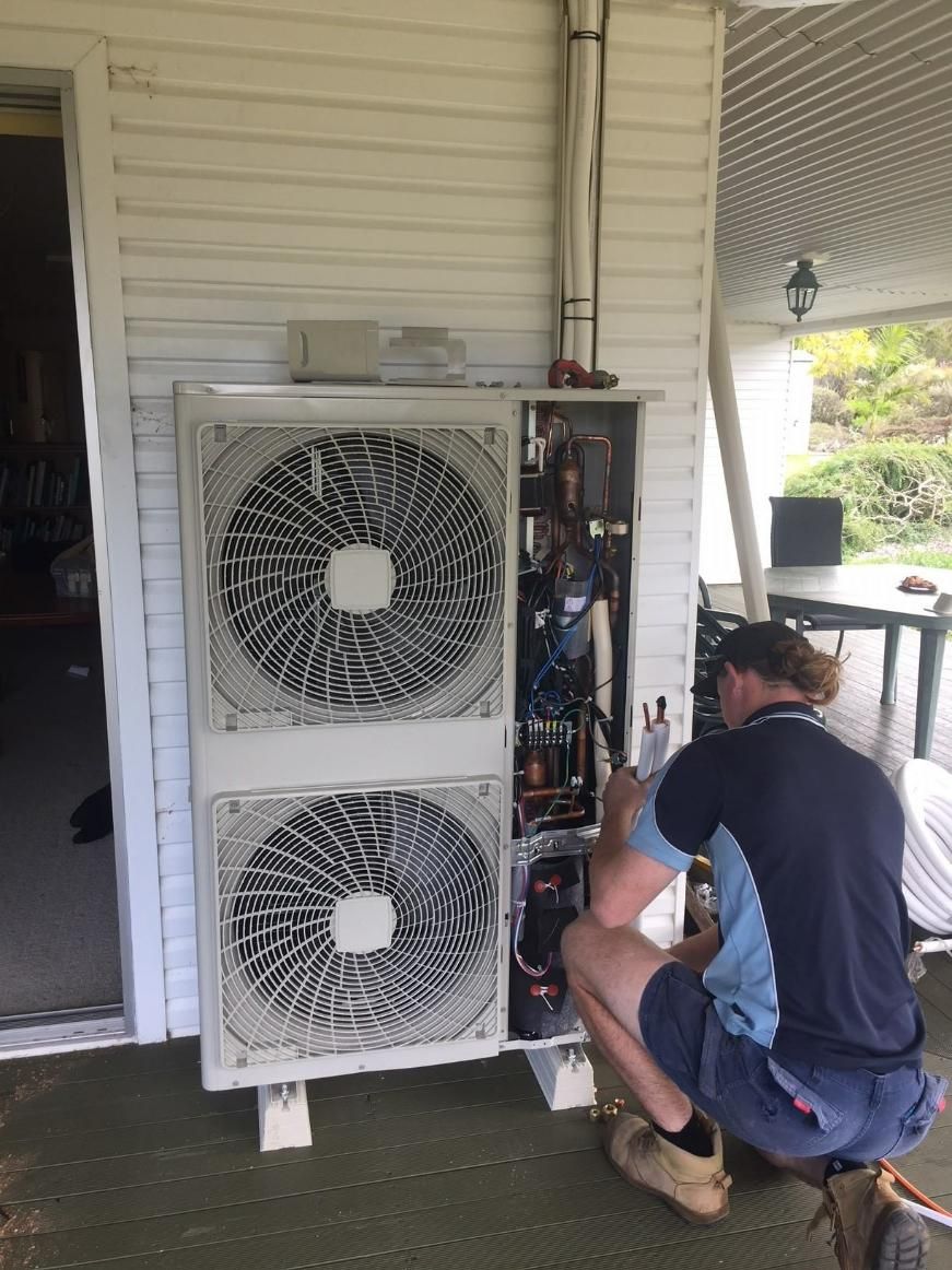 A Man Is Working on An Air Conditioner Outside of A House — Northernair in Ballina, NSW