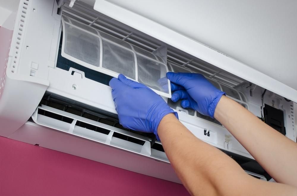 A Person Wearing Blue Gloves Is Cleaning an Air Conditioner — Northernair in Kyogle, NSW