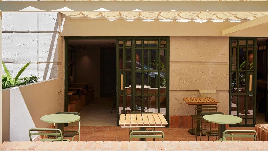 Terraza con mesas y sillas bajo un toldo, conectada a un espacio interior a través de puertas de vidrio