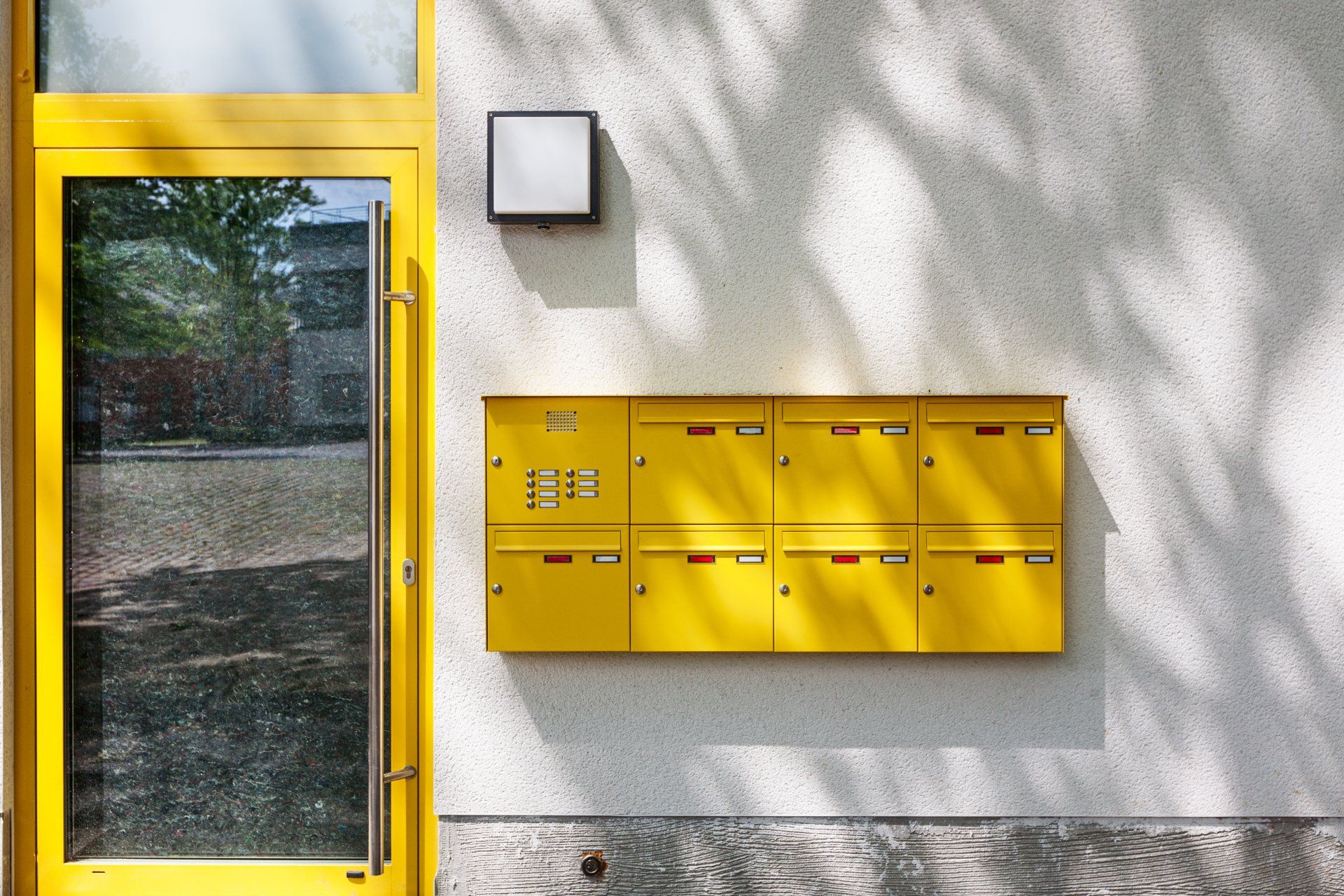 Gelbe Briefkästen an einer Hauswand befestigt neben gelber Haustüre.