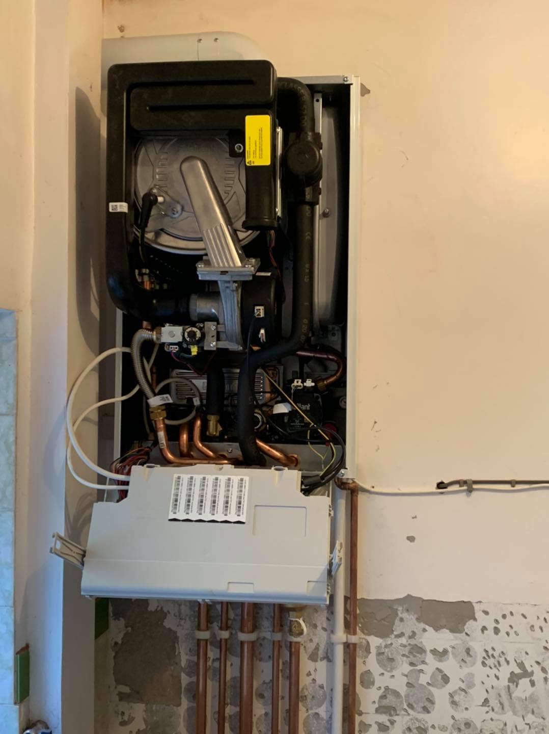 A wall-mounted gas boiler with copper pipes, wiring, and other internal components exposed.