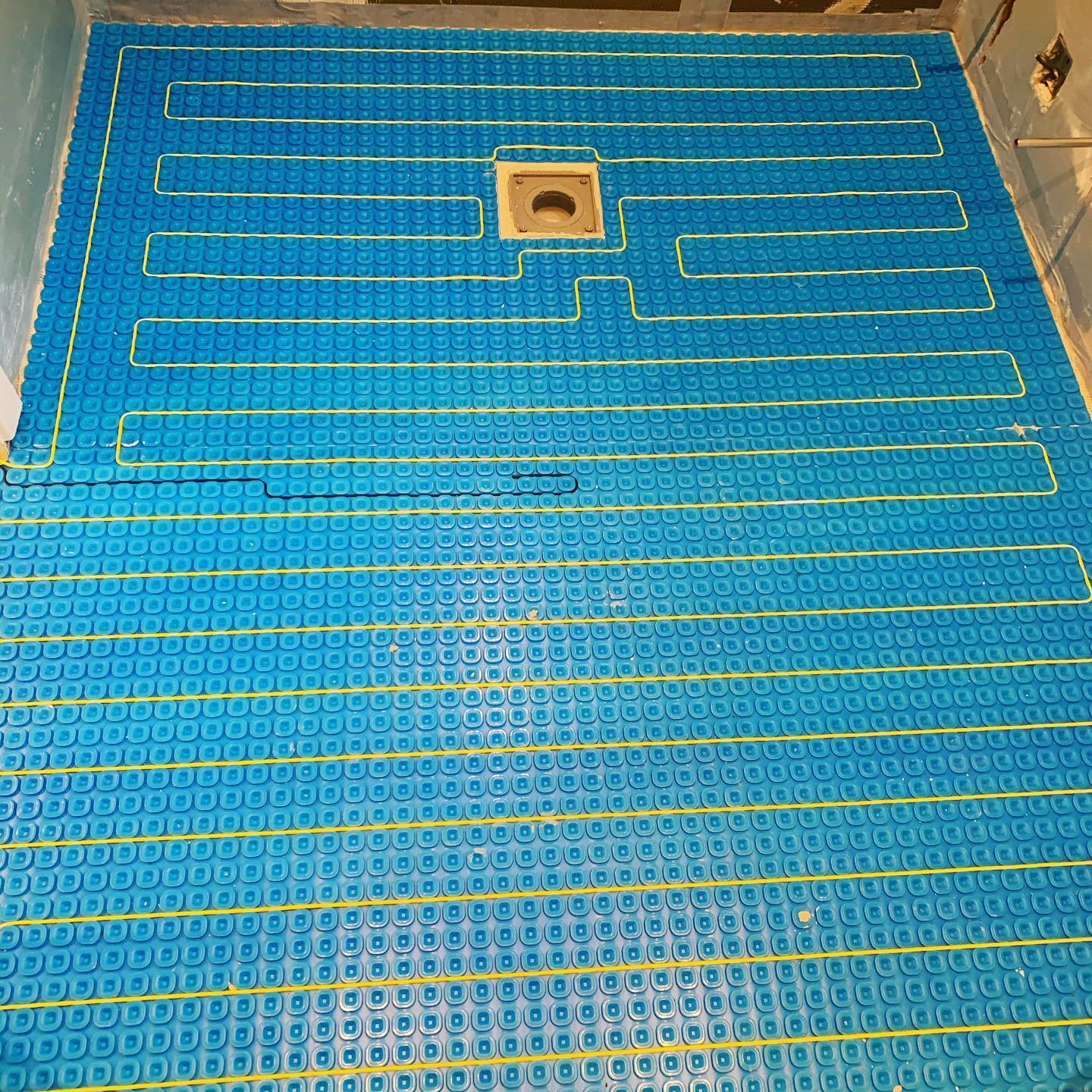 Blue, grid-patterned underfloor heating system installed in a bathroom, with a central drain.
