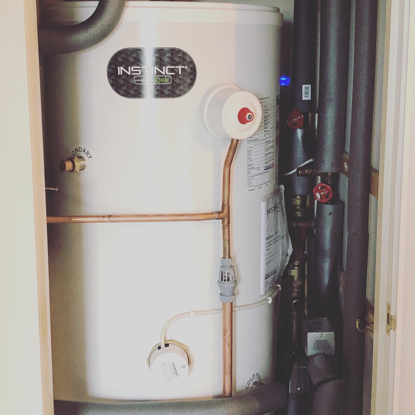 White water heater in a closet with copper pipes and black insulation.