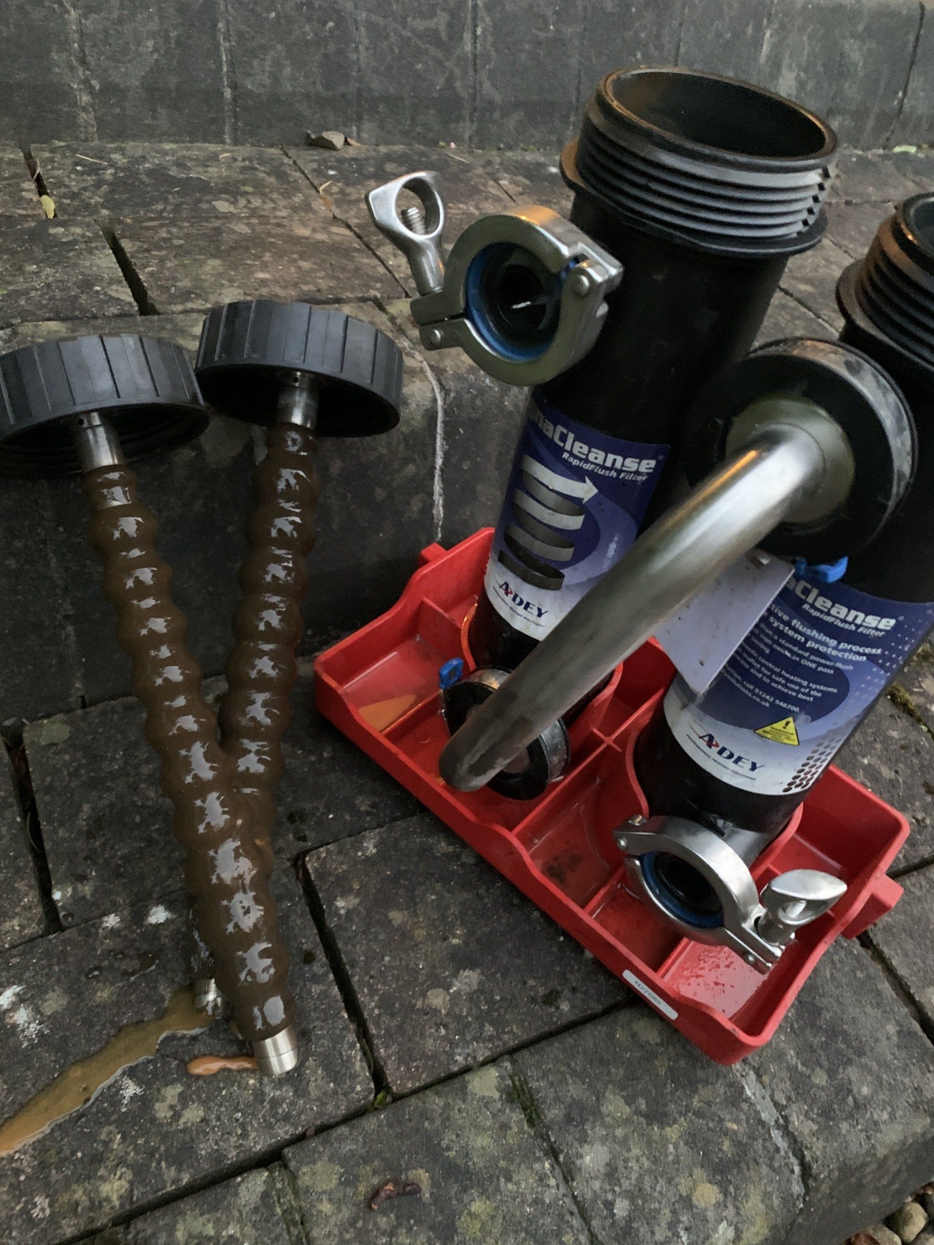 Black and silver industrial filter components, some assembled, rest on a red tray and brick surface outdoors.