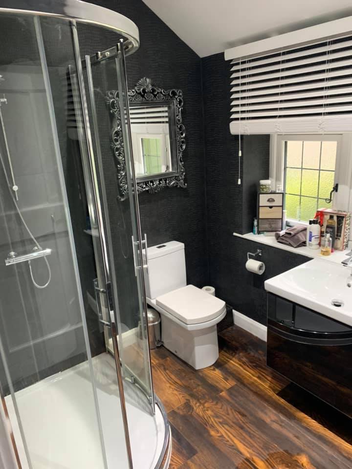 Bathroom with a black wall, a shower, a toilet, a sink, and a window with blinds.