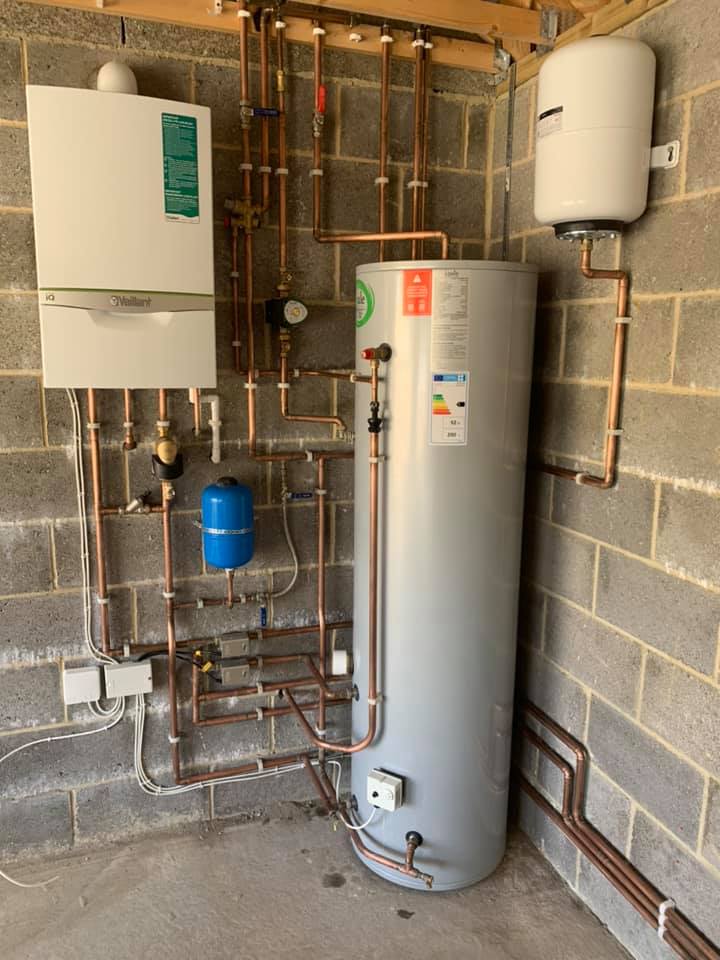 Copper pipes, boiler, and hot water tank installed on a concrete block wall.