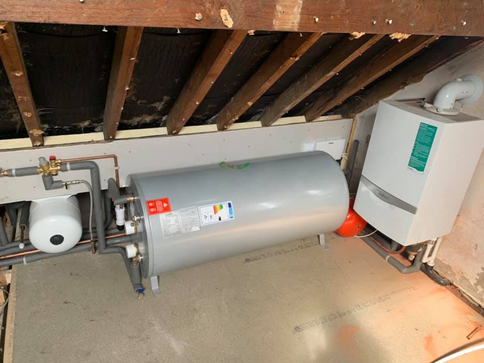 A water heater, boiler, and expansion tank installed in an attic. Piping connects the components.