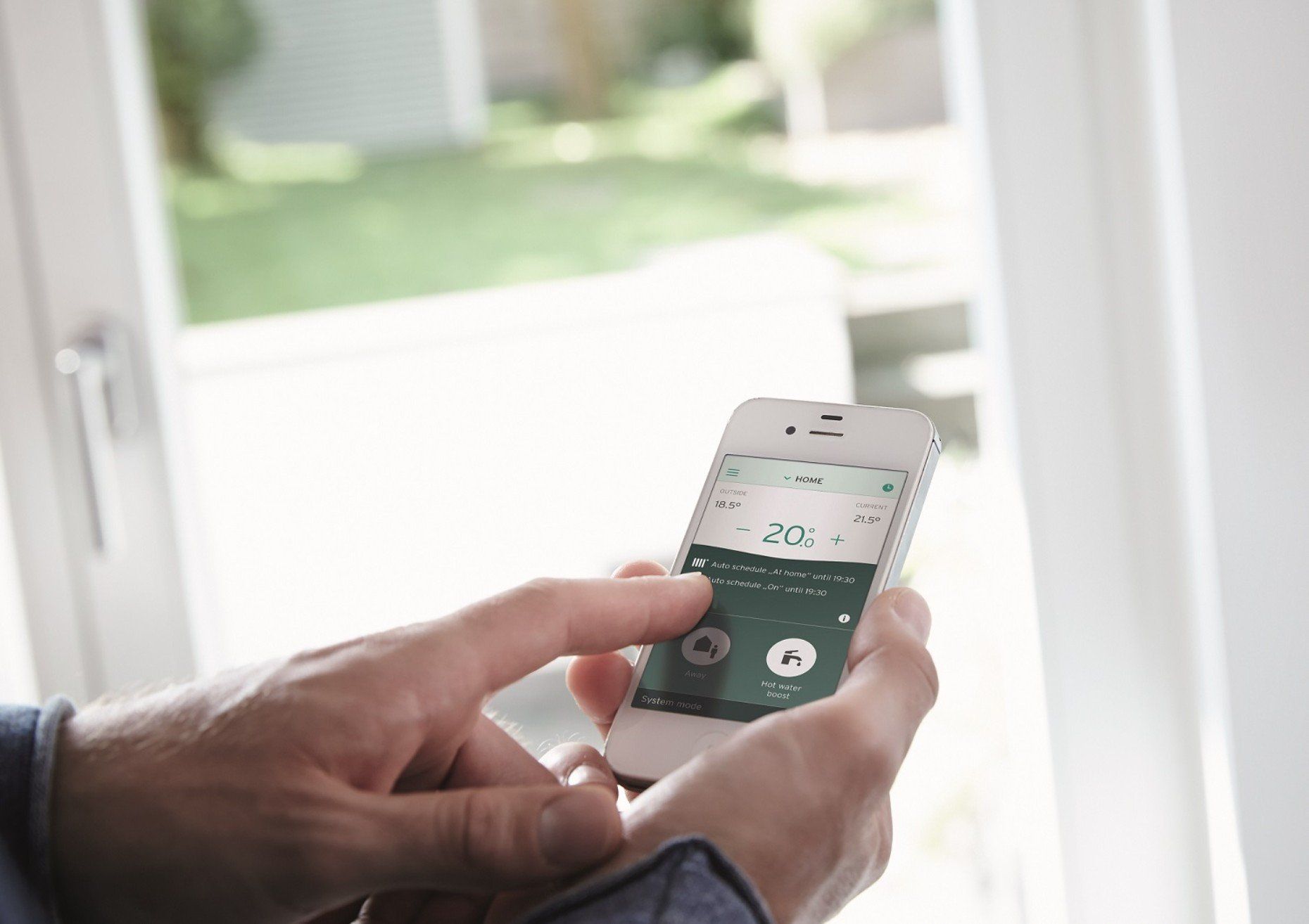 Person using a smartphone near a window, likely to control a smart home system.